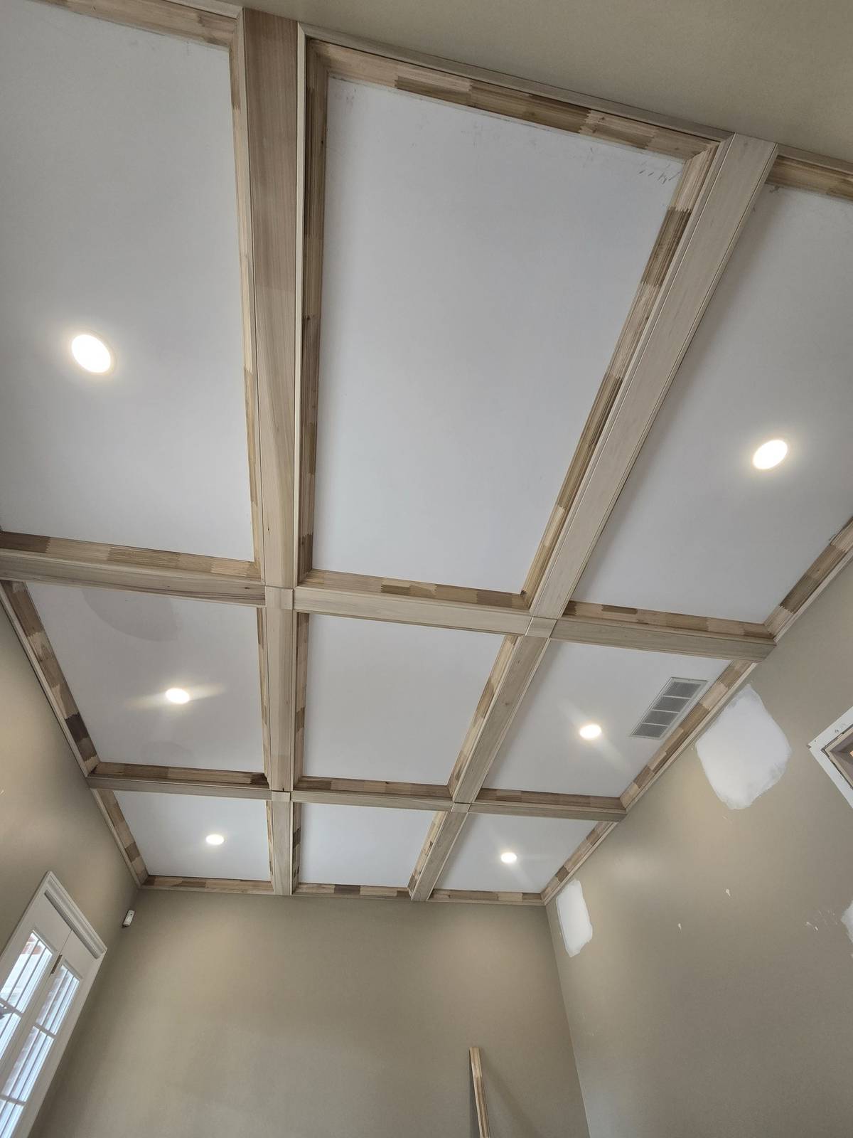 Coffered ceiling with wood beam trim and recessed lighting during finishing